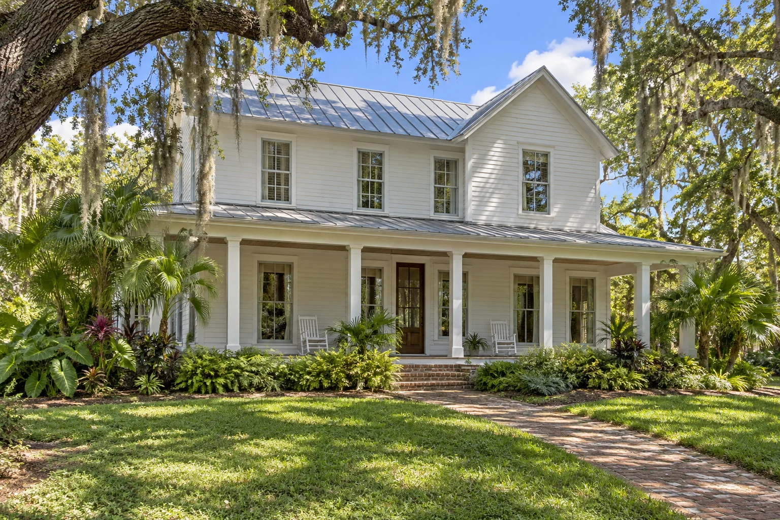 Two-story white Old Florida home with lap siding, a metal roof, and a deep porch beneath live oaks.