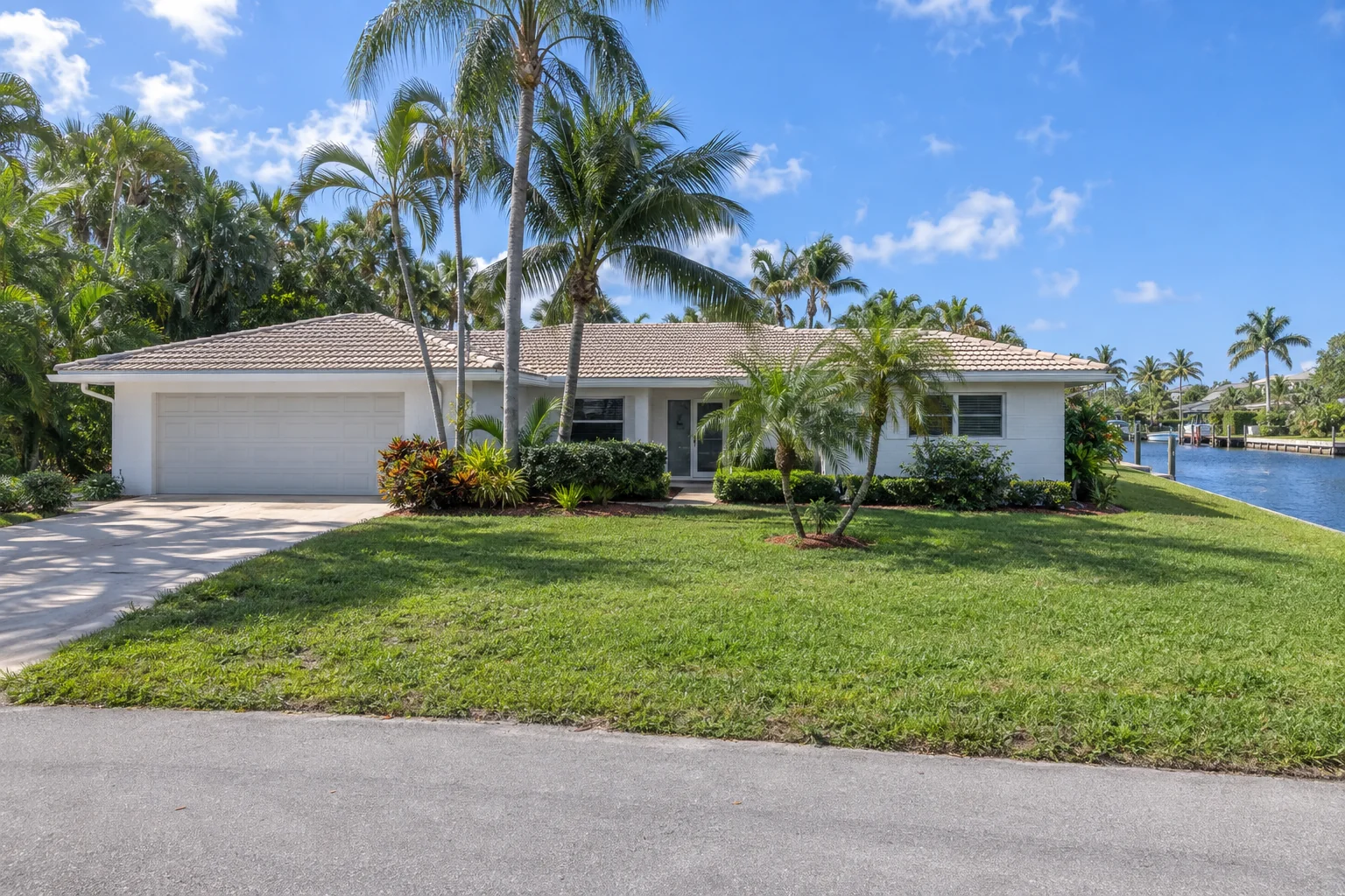 White 1980s ranch home with a flat tile roof and a canal beside the property.