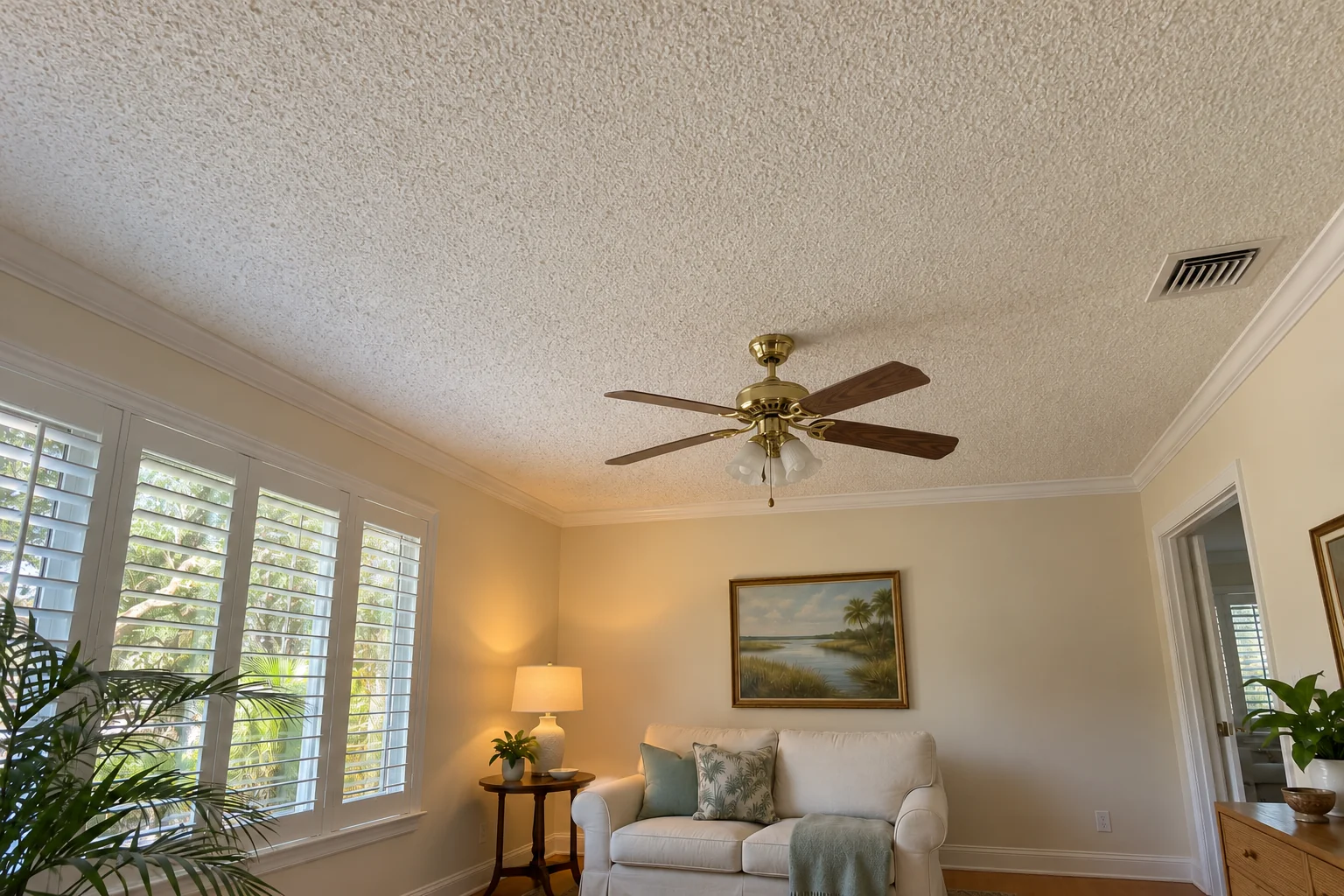 Small den with a yellowed popcorn ceiling and brass fan.