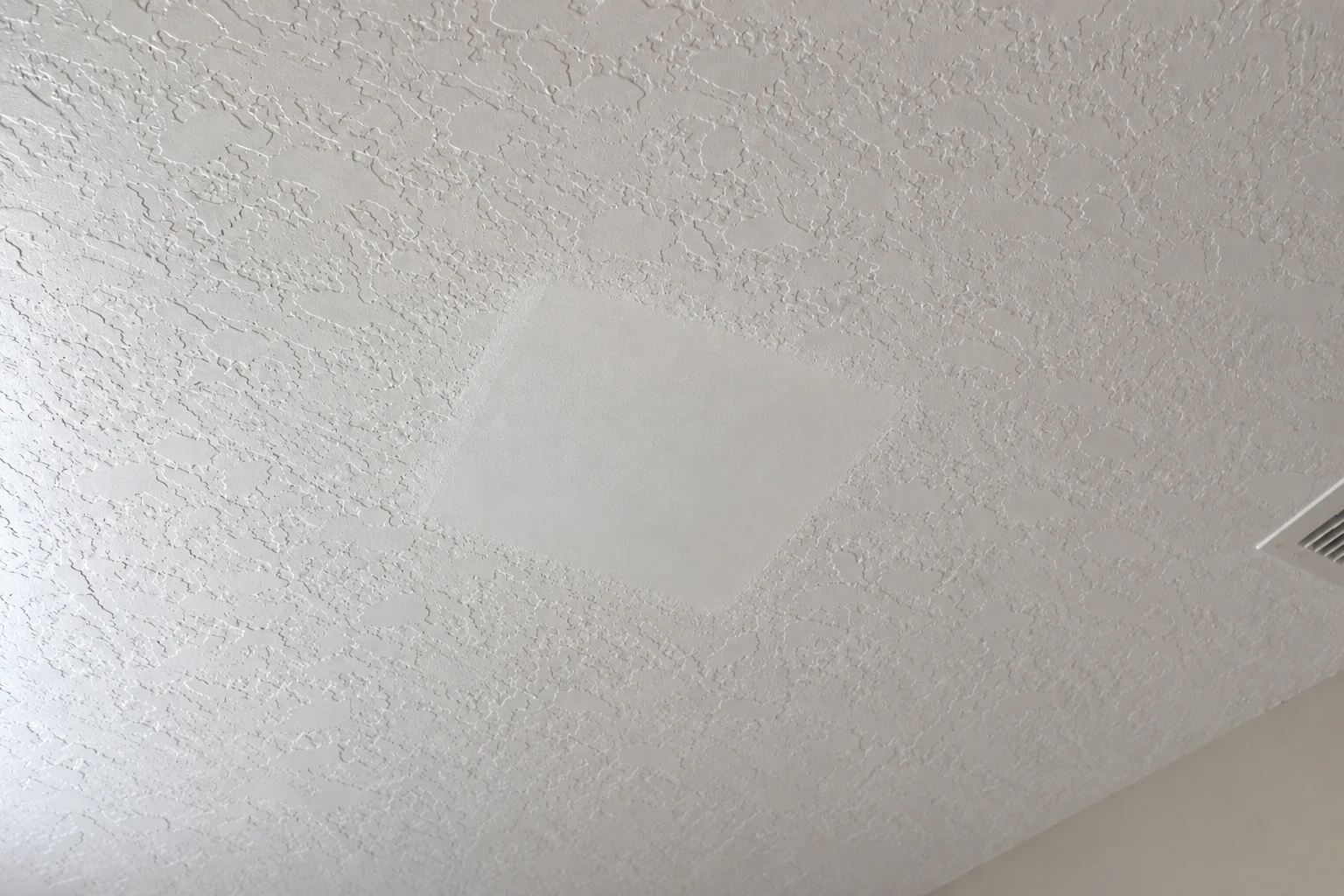 Smooth square patch surrounded by knockdown ceiling texture.